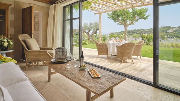Un patio amplio con una mesa de comedor, sillas de mimbre y vistas a un jardín exuberante y colinas lejanas.