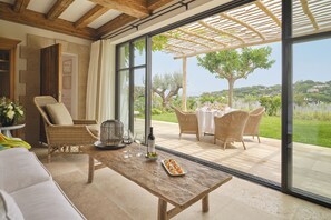 Un patio amplio con una mesa de comedor, sillas de mimbre y vistas a un jardín exuberante y colinas lejanas.