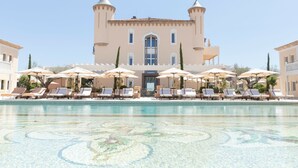 Una piscina grande con sillones de descanso y sombrillas, un edificio con dos torres y un cielo despejado.