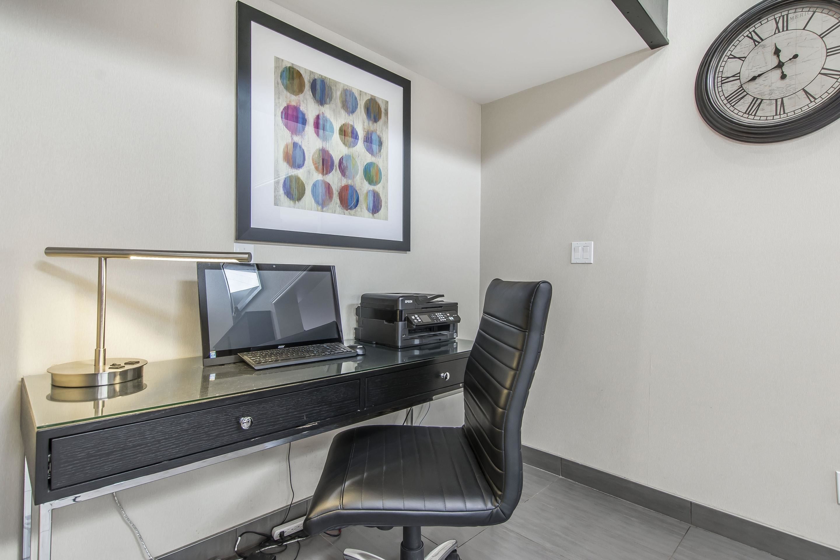 A modern office space with a desk, chair, computer, printer, and framed artwork on the wall.