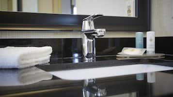 Un lavabo de salle de bain moderne avec un robinet chromé, une serviette blanche et deux flacons de produits de toilette posés sur le comptoir.
