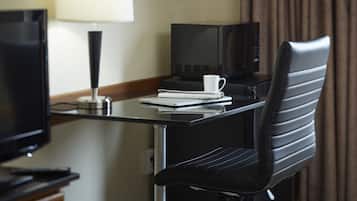 A hotel room with a desk, a laptop, a coffee cup, a remote control, and a television.