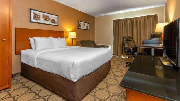 A hotel room with a large bed, a desk with a flat-screen TV, a chair, and two lamps.