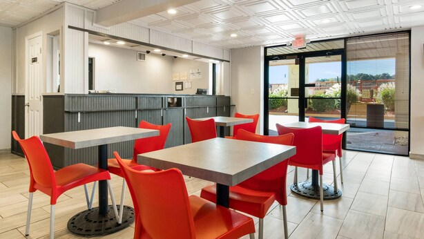 A modern restaurant with red chairs and grey tables, a kitchen area, and a view through large windows. - Econo Lodge Conyers (Conyers)
