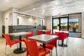 A modern restaurant with red chairs and grey tables, a kitchen area, and a view through large windows. - Econo Lodge Conyers (Conyers)