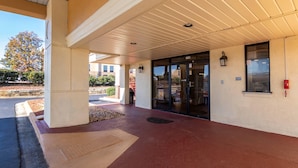 A covered entrance with a red-tiled floor, a glass door, and a wall-mounted light fixture. - Econo Lodge Conyers (Conyers)
