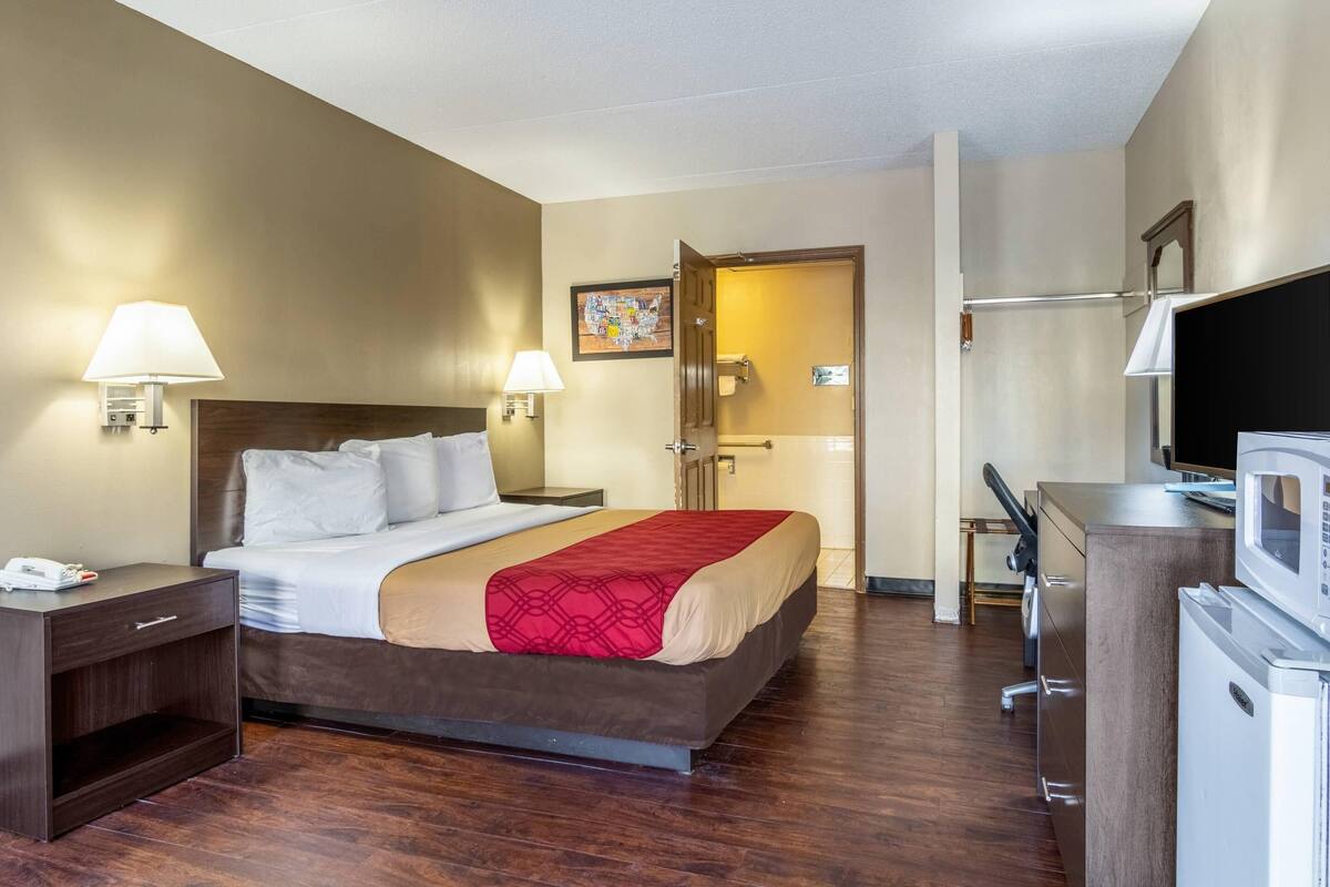 A hotel room with a bed, bedside lamps, a desk with a computer, a TV, and a microwave.