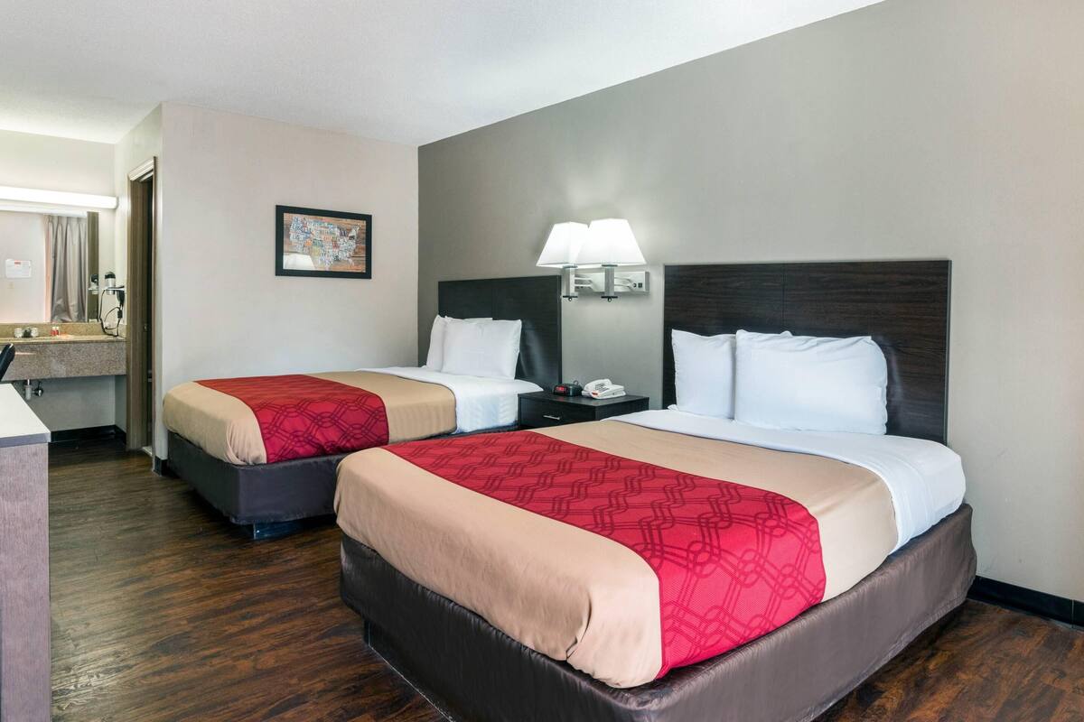 A hotel room with two beds, a nightstand, a lamp, a mirror, and a framed picture on the wall.