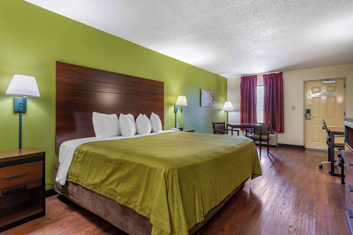 A hotel room with a large bed, two bedside tables with lamps, a desk with a chair, and a door.