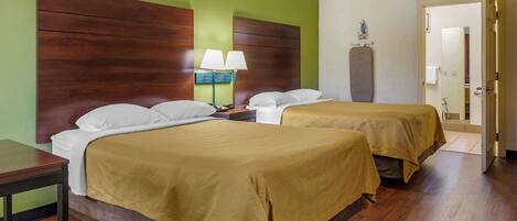A hotel room with two beds, a nightstand with a lamp, and a wooden headboard.
