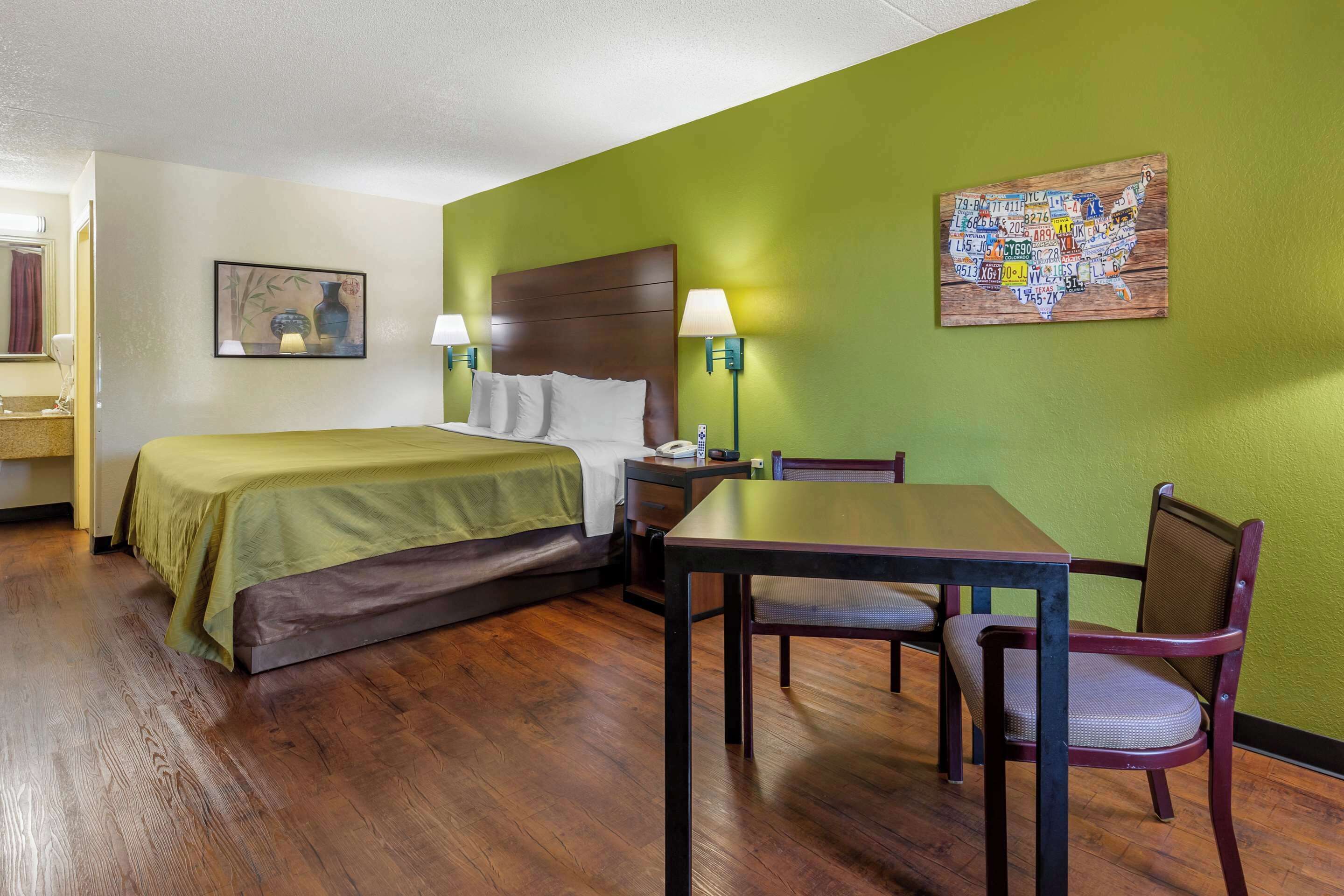Habitación de hotel con cama, escritorio y silla. Hay un cuadro en la pared y un mapa de Estados Unidos.