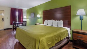 Une chambre d’hôtel avec un grand lit, une table de chevet en bois, un bureau avec une chaise et un mur vert.
