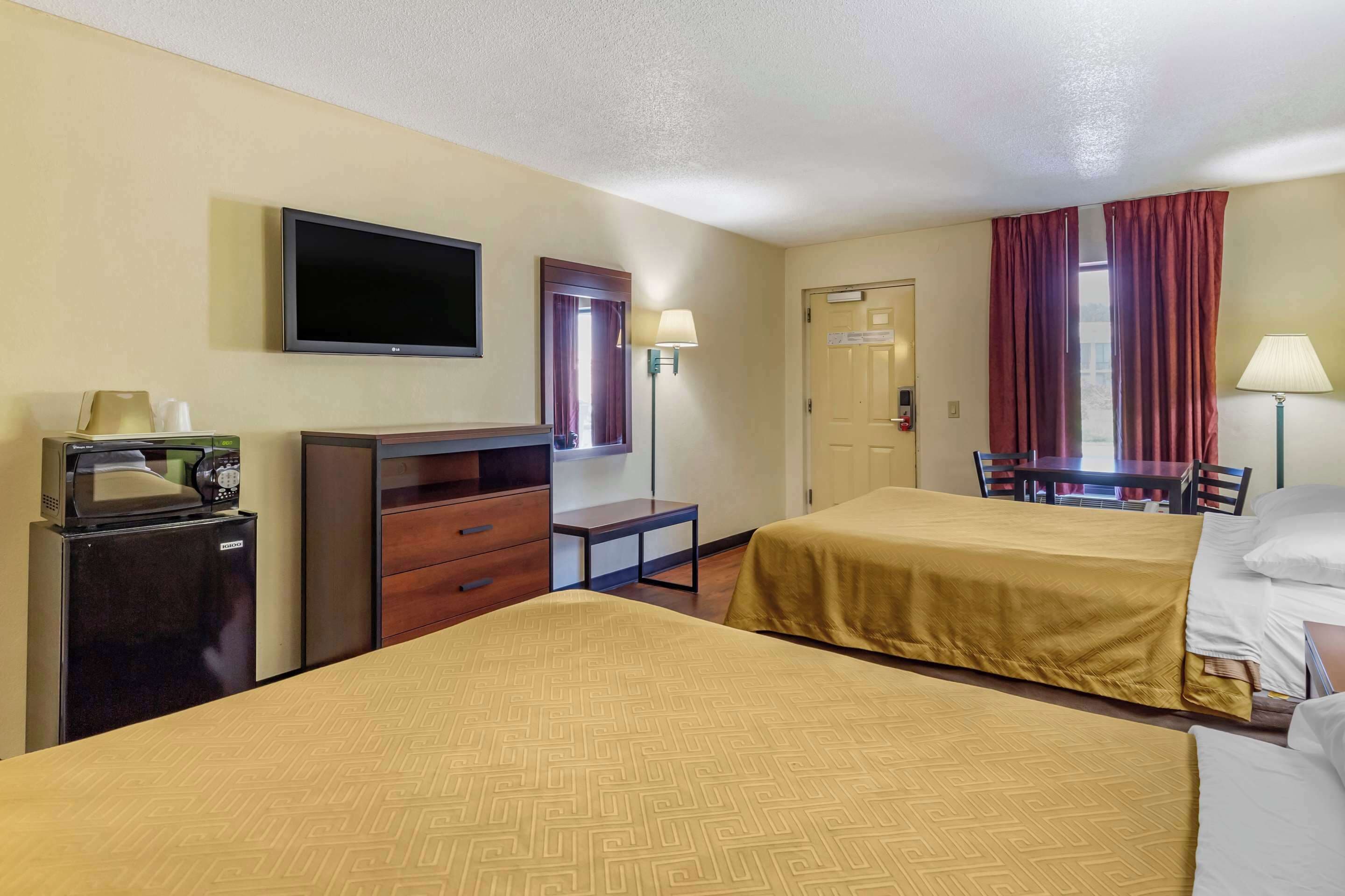 Een hotelkamer met twee bedden, een televisie, een bureau met lamp, een koelkast en een deur.