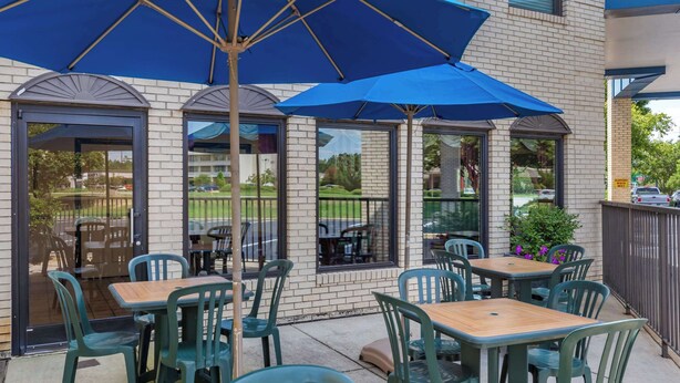 Un espace extérieur aménagé en terrasse, avec des tables et des chaises, protégé par des parasols bleus, et un bâtiment en briques en arrière-plan.