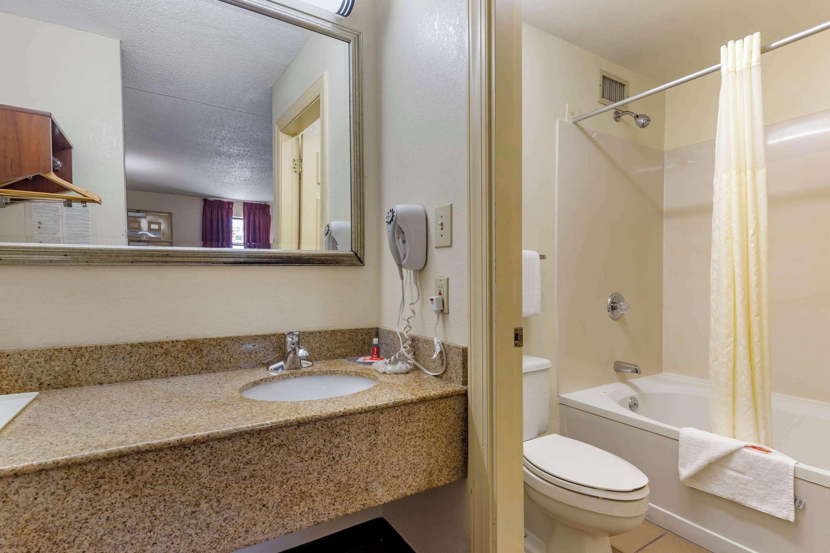 A bathroom with a granite countertop sink, a toilet, a bathtub, and a shower curtain.