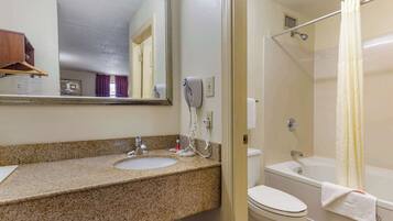 A bathroom with a granite countertop sink, a toilet, a bathtub, and a shower curtain.