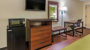 Une chambre d’hôtel équipée d’une télévision à écran plat, d’un four à micro-ondes, d’un bureau en bois avec des tiroirs, d’une chaise et d’une lampe.