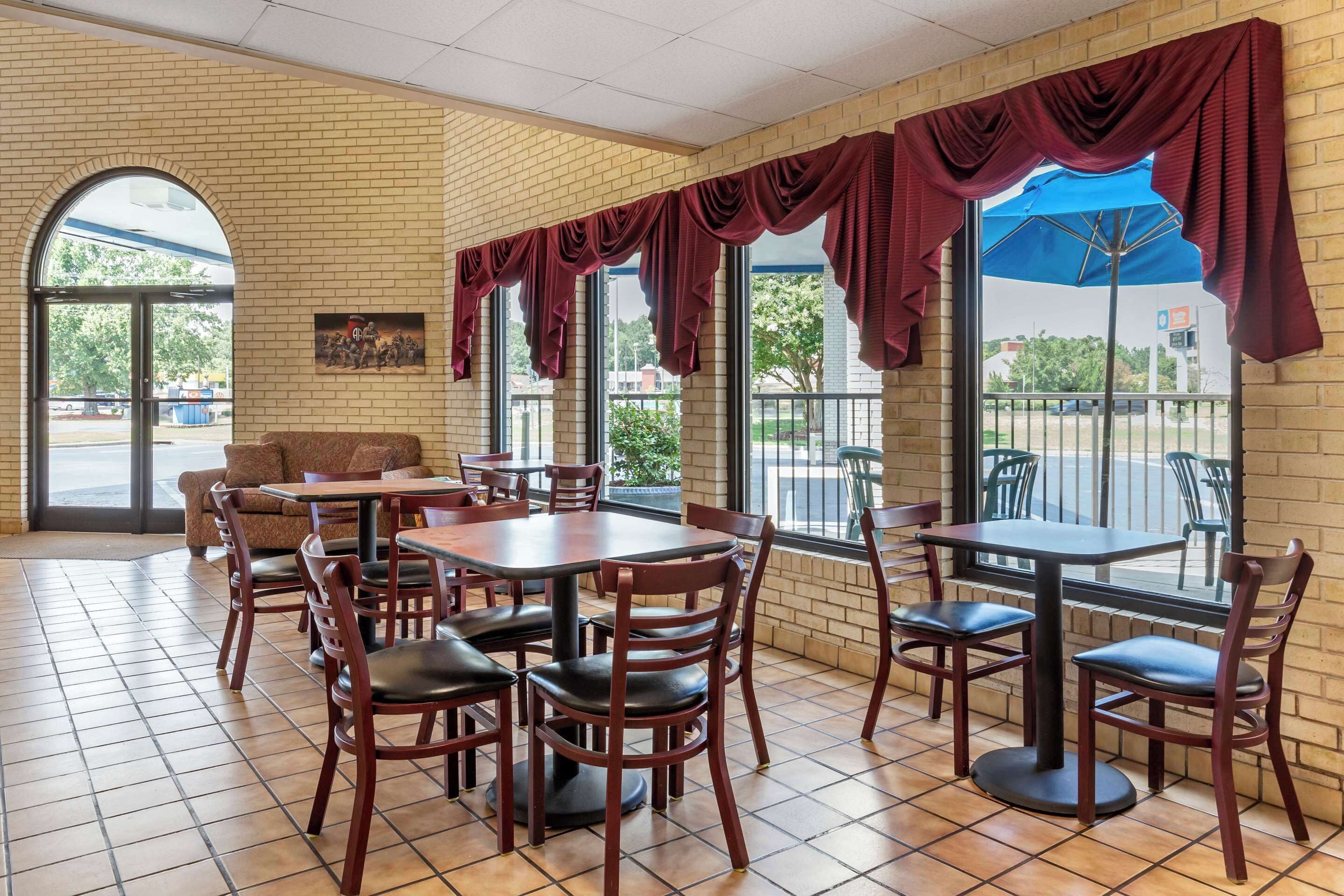 A restaurant with brick walls, large windows, and red curtains. Tables and chairs are arranged for dining.
