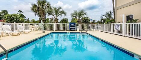 A swimming pool with white lounge chairs and a white fence.