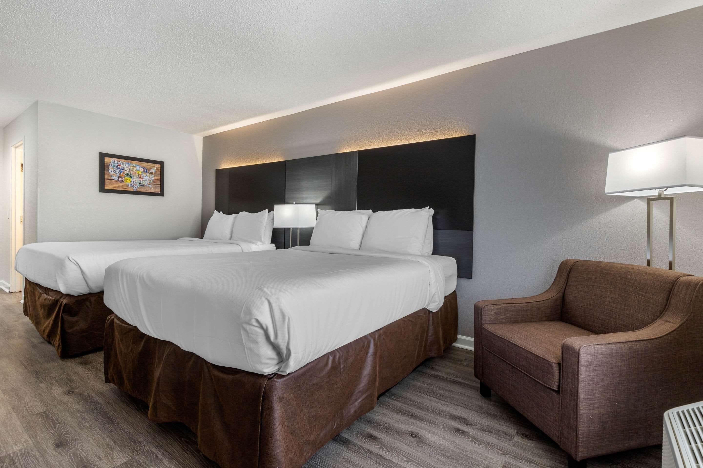 A hotel room with two beds, a sofa, a lamp, and a painting on the wall.