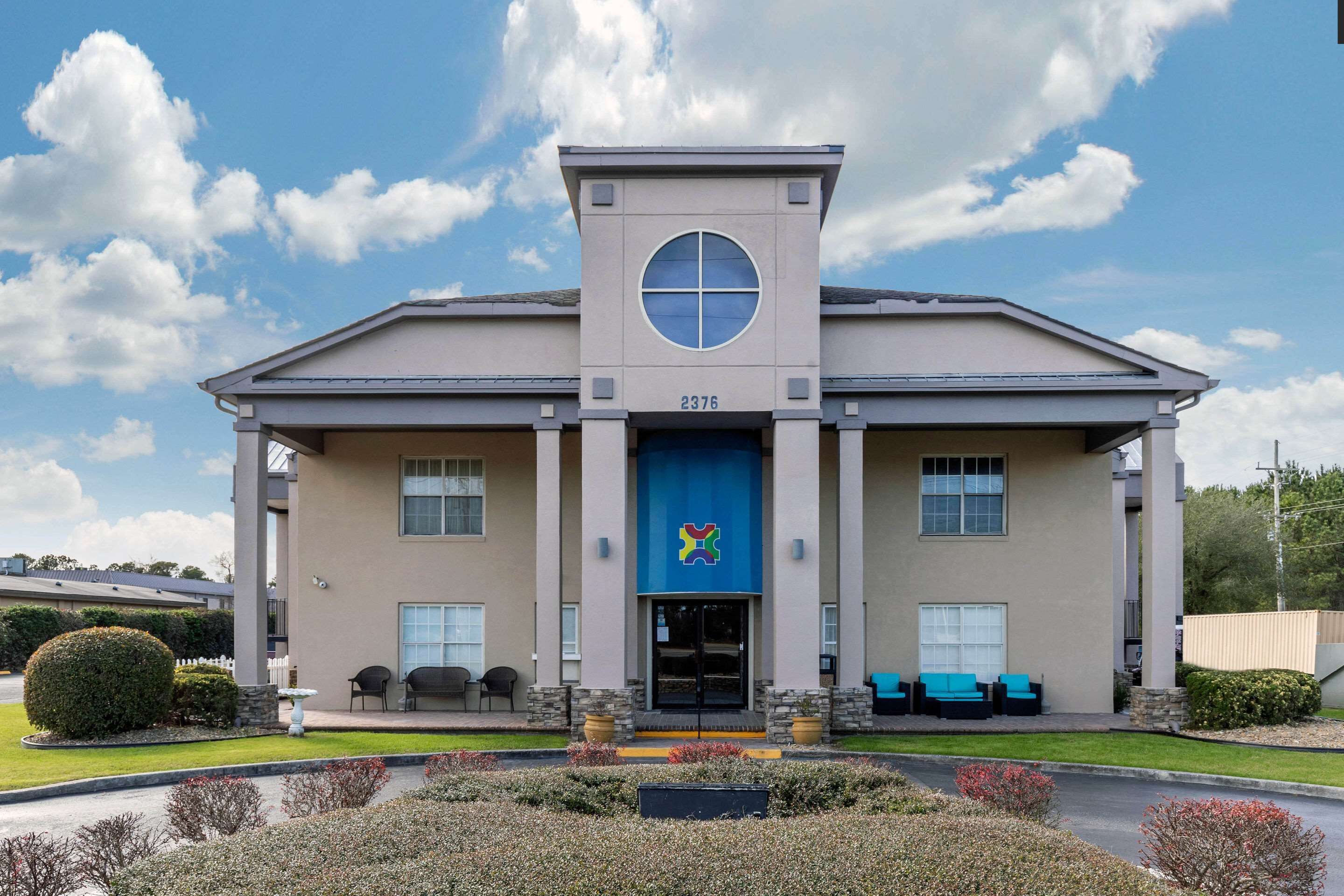 A building with a central entrance, columns, and a blue awning with a logo.