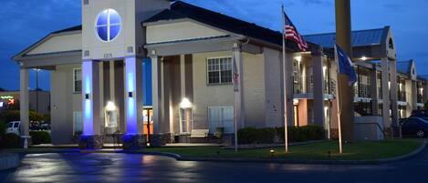 Een hotel met een opvallende ingang, een vlaggenmast met de Amerikaanse vlag, en een goed verlichte gevel.