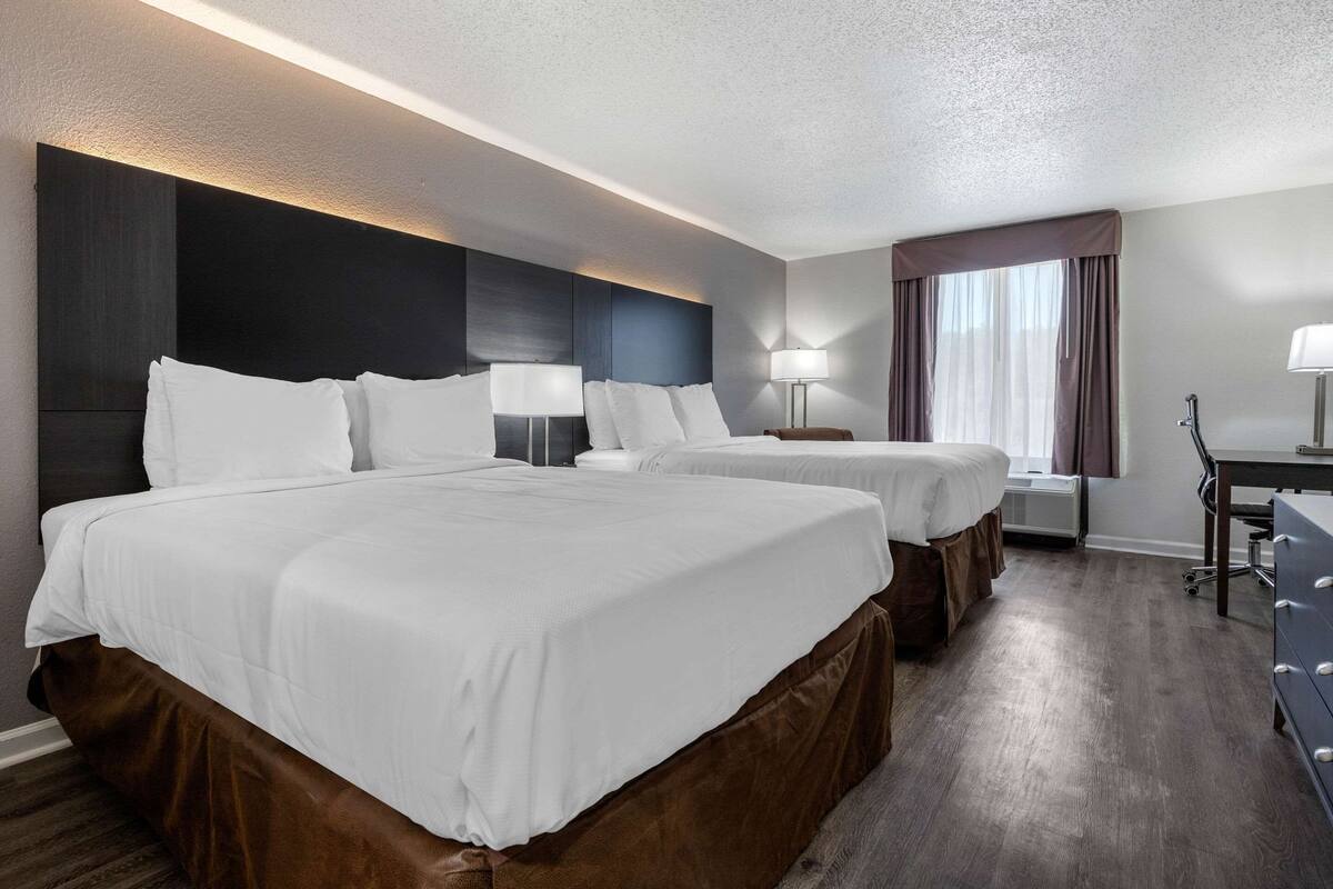 A hotel room with two beds, a desk, and a window with curtains.
