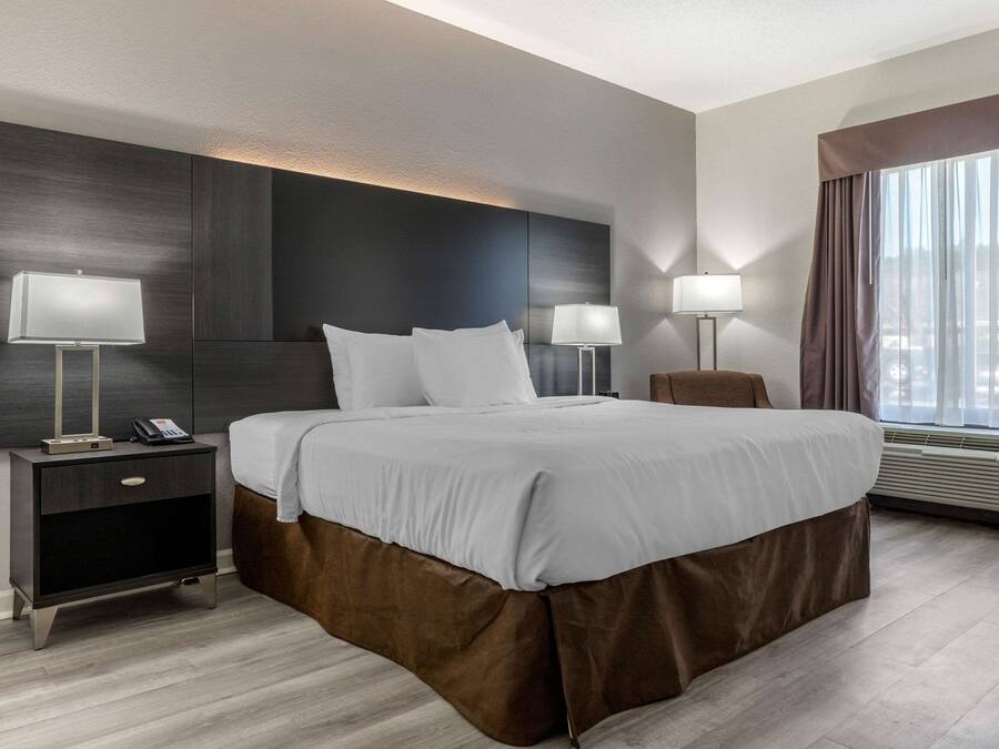 A modern hotel room with a large bed, bedside lamps, a nightstand, and a window with curtains.