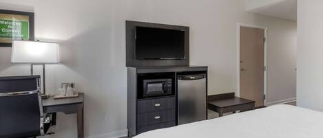 Una habitación de hotel con una cama, un escritorio con computadora, televisor, microondas y puerta.