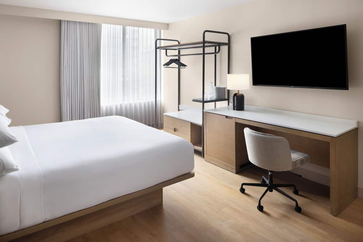 A hotel room with a bed, desk, chair, TV, and curtains.