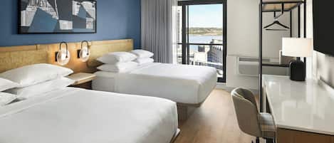 Habitación de hotel con dos camas, un escritorio, una silla, un ventanal con vistas y un televisor montado en la pared.