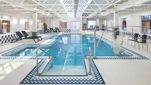An indoor swimming pool with a checkered floor pattern, lounge chairs, and a high ceiling with a truss structure.