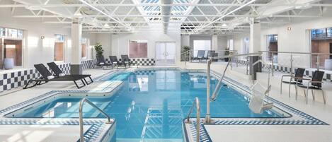 Piscina interior com padrão de piso quadriculado, espreguiçadeiras e teto alto com estrutura de treliça.