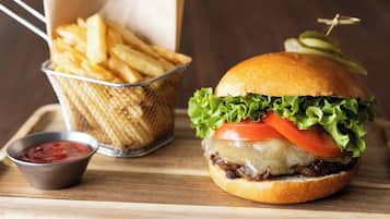 A burger with lettuce, tomato, and cheese, a basket of fries, and a small container of ketchup on a wooden surface.