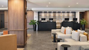 A modern hotel lobby with a reception desk, seating area, and a large plant.