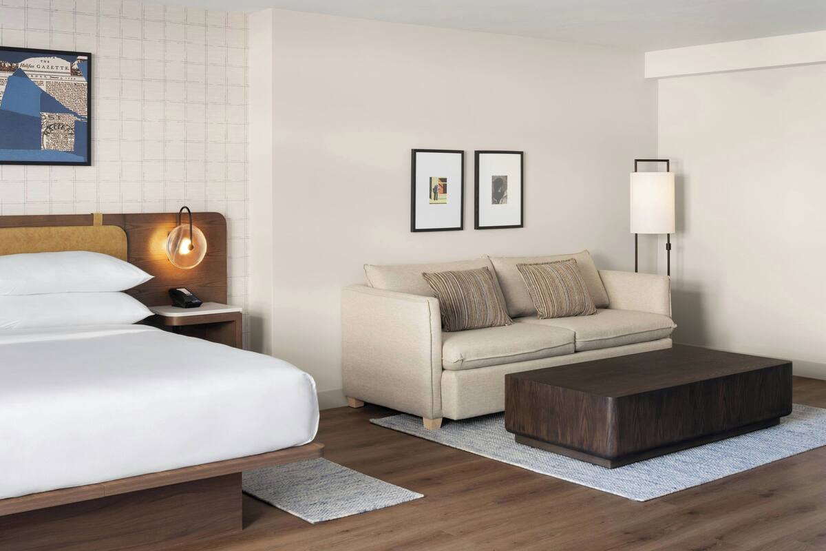 A hotel room with a bed, a sofa, a coffee table, a nightstand, a lamp, and framed pictures on the wall.