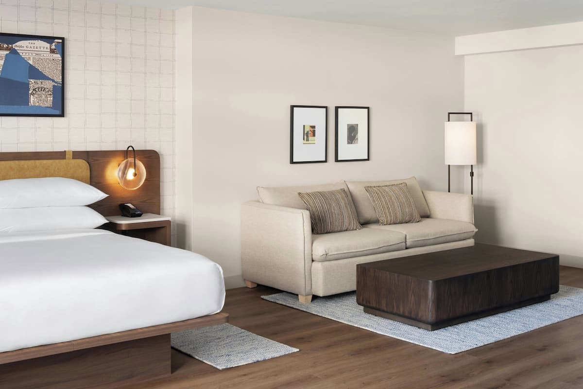 A hotel room with a bed, a sofa, a coffee table, a nightstand, a lamp, and framed pictures on the wall.