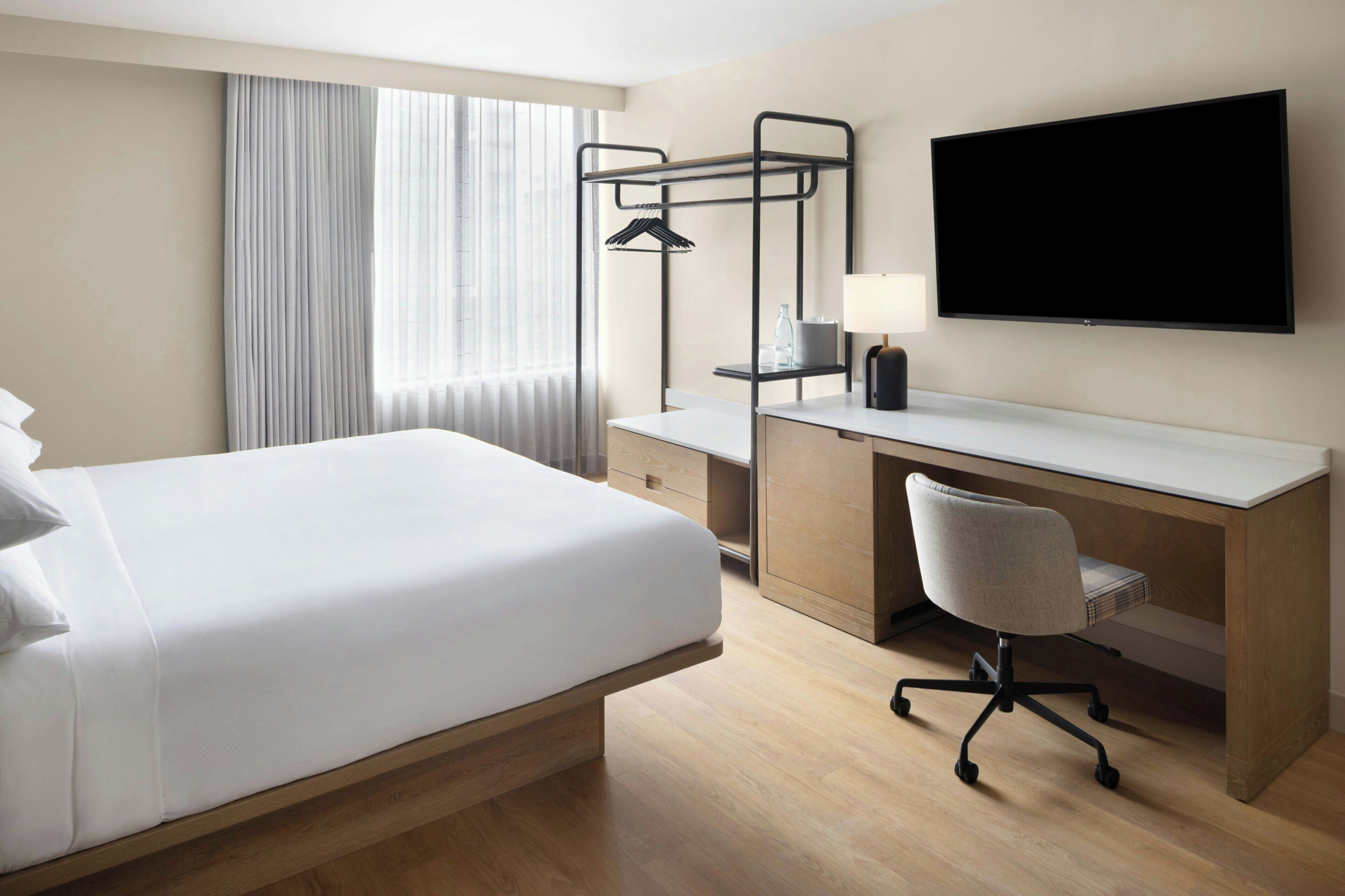 Ein Hotelzimmer mit Bett, Schreibtisch, Stuhl, Fernseher und einem Fenster mit Vorhängen.