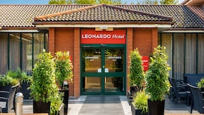 El exterior del Hotel LEONARDO, con techo de tejas, puertas dobles y plantas en macetas.