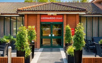 El exterior del Hotel LEONARDO, con techo de tejas, puertas dobles y plantas en macetas.