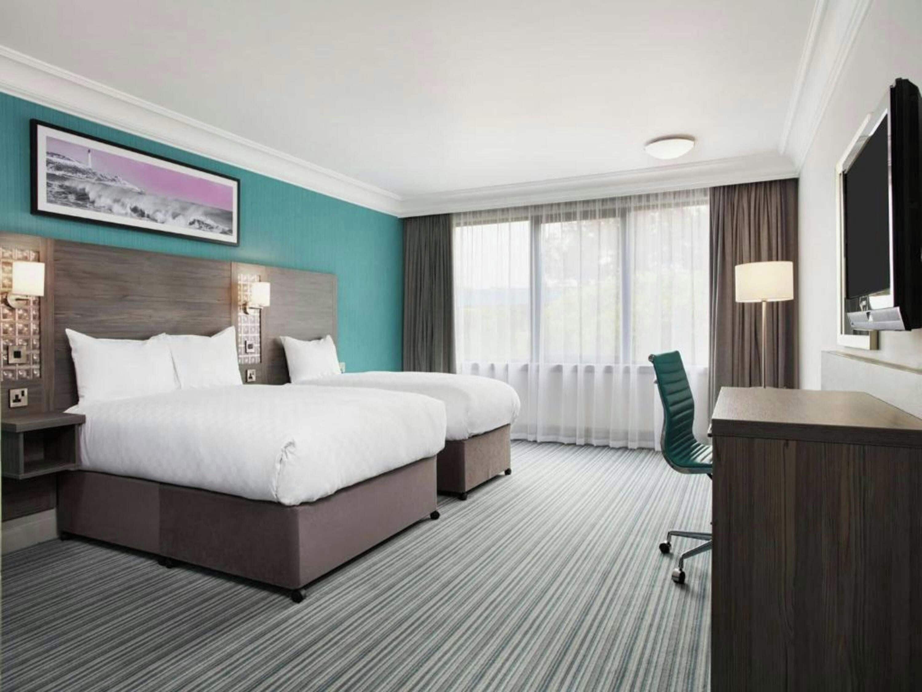 A hotel room with a large bed, a desk, a chair, and a window with curtains.