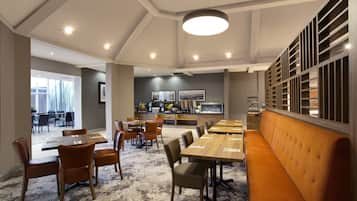 A modern restaurant with a long counter, multiple dining tables, and a seating area with a bench.