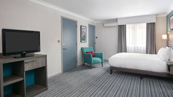 A hotel room with a bed, a television, a chair, and a door.