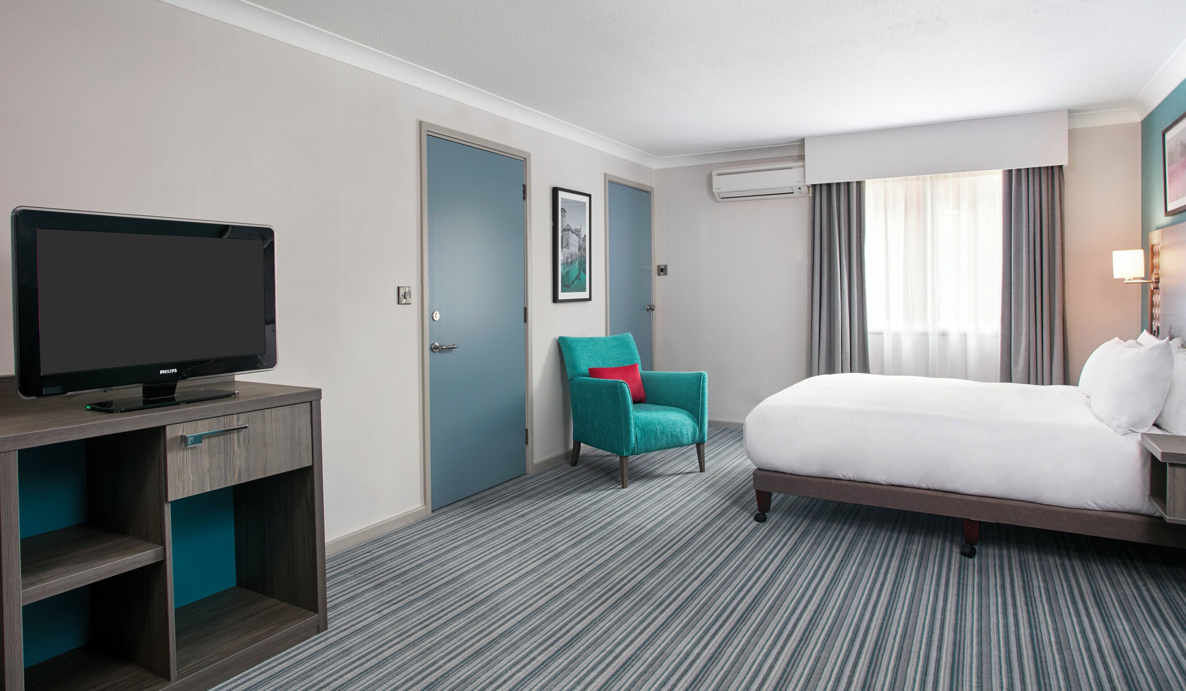 A hotel room with a bed, a television, a chair, and a door.