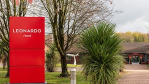 Un letrero rojo del Hotel Leonardo con un edificio de ladrillo en el fondo.