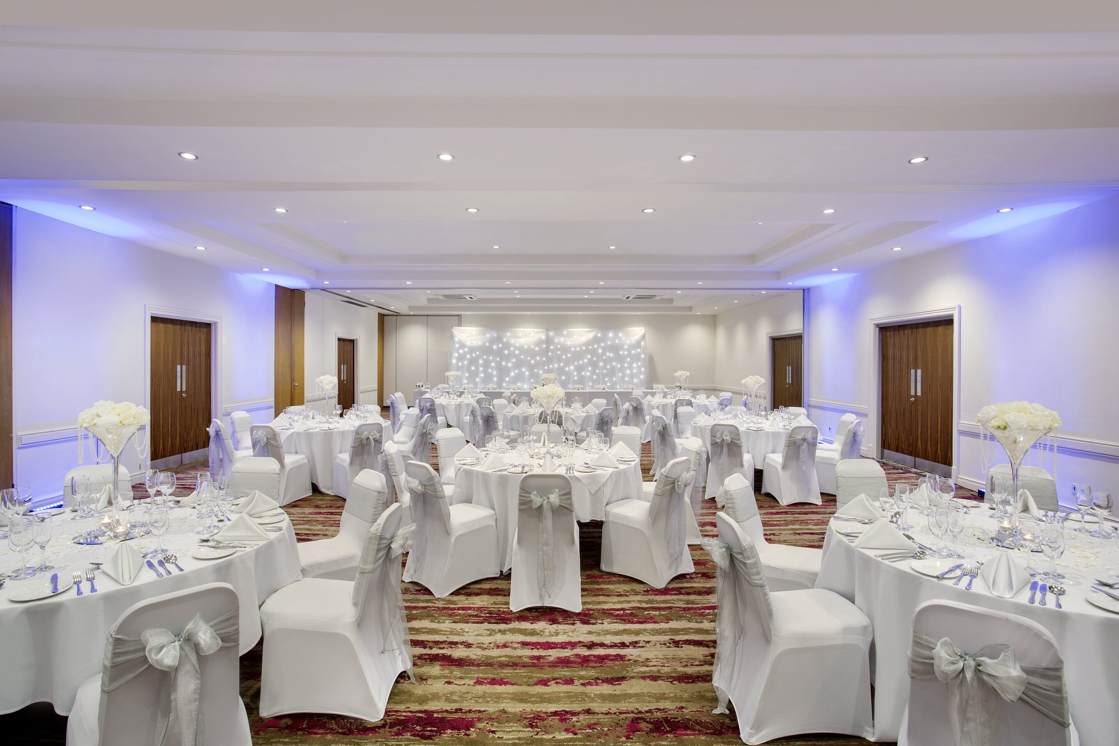 A banquet hall with round tables, white tablecloths, and chairs with white covers.
