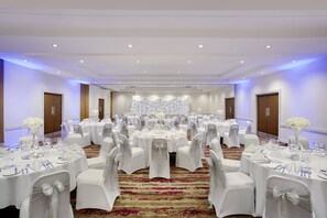 Un salón de banquetes con mesas redondas, manteles blancos y sillas con fundas blancas.