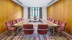 Un salón de conferencias con una larga mesa, sillas estampadas y vistas amplias a través de grandes ventanales.