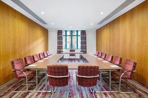 Un salón de conferencias con una larga mesa, sillas estampadas y vistas amplias a través de grandes ventanales.