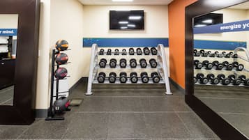 A gym with a wall-mounted TV, a rack of dumbbells, and a shelf with sports balls.